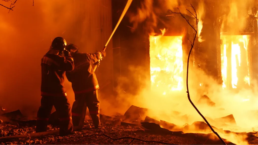 Bomberos lanzando agua a presión para sofocar un incendio voraz en una casa de noche.