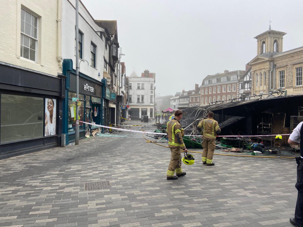 Bomberos inspeccionando los puestos calcinados y la zona acordonada tras el incendio en Kingston Market Place.