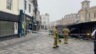 Bomberos inspeccionando los puestos calcinados y la zona acordonada tras el incendio en Kingston Market Place.
