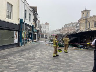 Bomberos inspeccionando los puestos calcinados y la zona acordonada tras el incendio en Kingston Market Place.