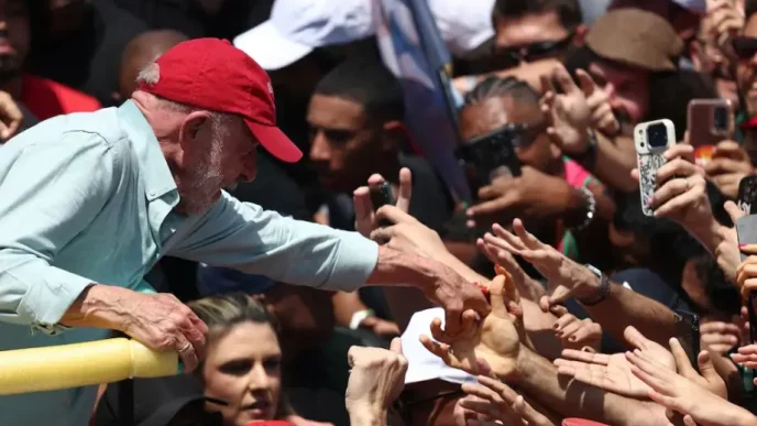 Luiz Inácio Lula da Silva con gorra roja estrechando la mano de sus seguidores en un acto multitudinario.