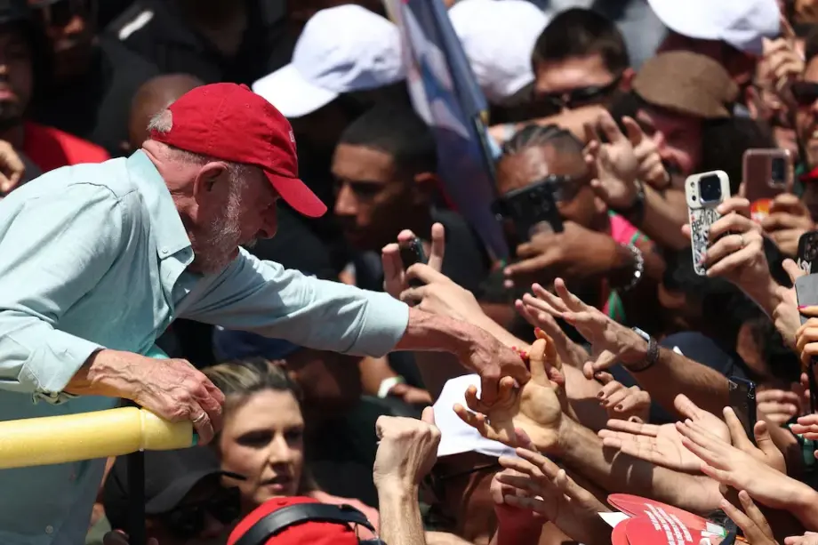 Luiz Inácio Lula da Silva con gorra roja estrechando la mano de sus seguidores en un acto multitudinario.