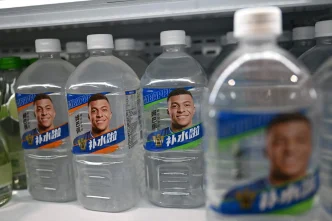Botellas de agua en un estante de supermercado con la cara impres de Kylian Mbappé en la etiqueta.