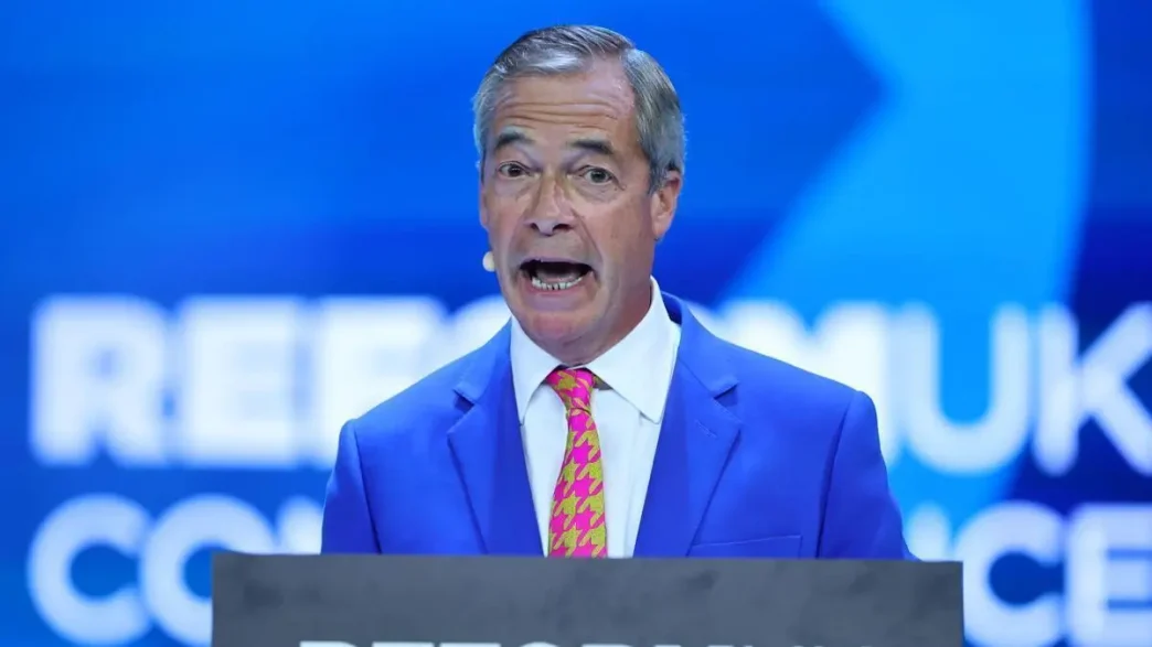 Nigel Farage hablando en un atril azul durante un evento político del Partido Reformista.