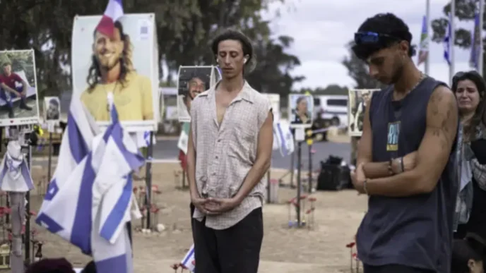 ersonas guardando silencio en el memorial del festival Nova rodeadas de fotografías de las víctimas del 7 de octubre y banderas de Israel.