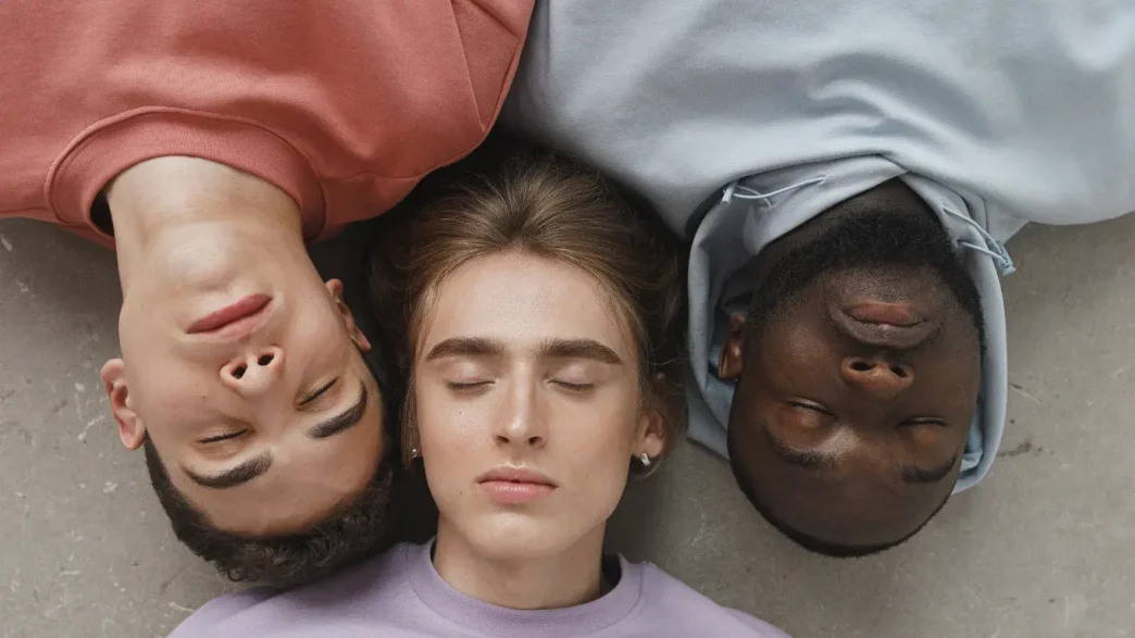 Tres jóvenes de diversas procedencias étnicas acostados juntos con los ojos cerrados.