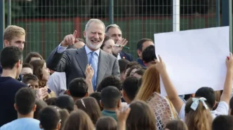 El Rey Felipe VI sonriente saludando rodeado de niños en el patio de un colegio.