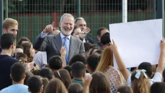 El Rey Felipe VI sonriente saludando rodeado de niños en el patio de un colegio.