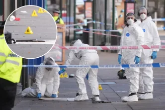 Agentes forenses vestida con trajes blancos de protección investigando la escena del tiroteo en Nottingham junto a un arma de fuego.