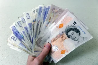 Mano sosteniendo un abanico de billetes de libras esterlinas británicas de diez y veinte libras.