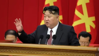 El líder norcoreano Kim Jong-un pronunciando un discurso desde un estrado con la mano levantada frente a banderas del partido.