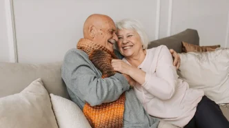 Pareja mayor de ancianos abrazándose sonrientes en el sofá del salón de su casa.