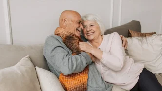 Pareja mayor de ancianos abrazándose sonrientes en el sofá del salón de su casa.