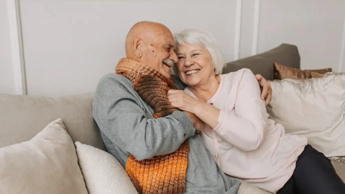 Pareja mayor de ancianos abrazándose sonrientes en el sofá del salón de su casa.