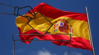 Ilustración de una mano introduciendo una papeleta en una urna electoral sobre la bandera de España ondeando al viento.