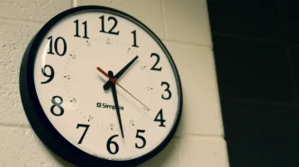 Reloj de pared analógico de esfera blanca y números negros colgado en una pared de ladrillo.