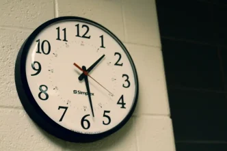 Reloj de pared analógico de esfera blanca y números negros colgado en una pared de ladrillo.