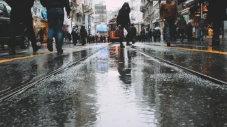 Peatones caminando por una calle comercial mojada por la lluvia con un tranvía al fondo.