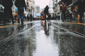 Peatones caminando por una calle comercial mojada por la lluvia con un tranvía al fondo.