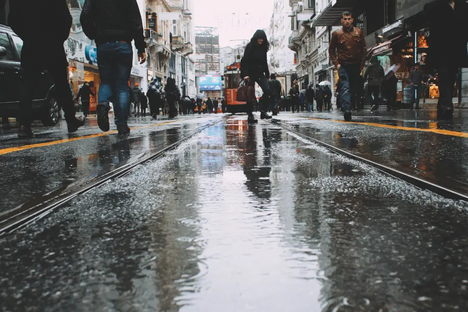 Peatones caminando por una calle comercial mojada por la lluvia con un tranvía al fondo.