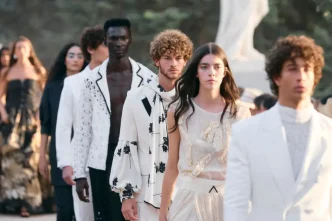 Modelos desfilaron en fila vistiendo conjuntos blancos y estampados sobre una pasarela al aire libre.