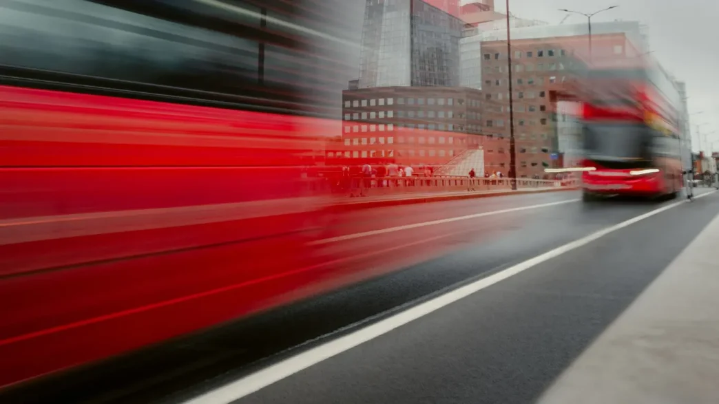 Autobús rojo de dos pisos transitando a gran velocidad por una avenida de Londres.