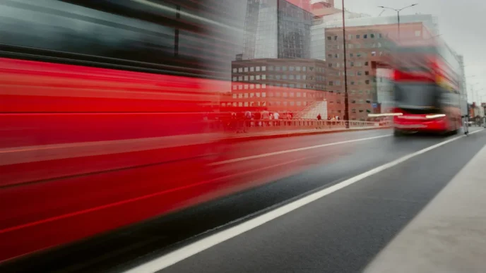 Autobús rojo de dos pisos transitando a gran velocidad por una avenida de Londres.