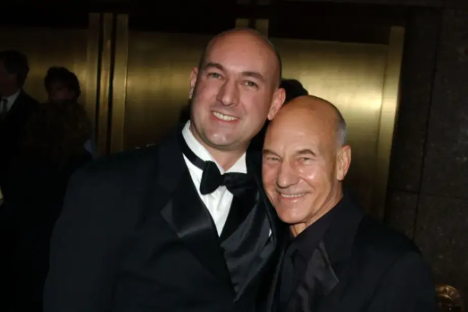 El actor Sir Patrick Stewart sonriendo junto a su hijo Daniel en una gala con esmoquin.