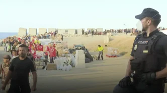 Agente de la Policía Nacional vigilando a un grupo de personas y voluntarios de Cruz Roja en la zona portuaria de Ceuta.