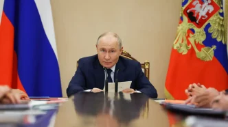 Vladimir Putin sentado en una mesa de reuniones con banderas rusas de fondo.