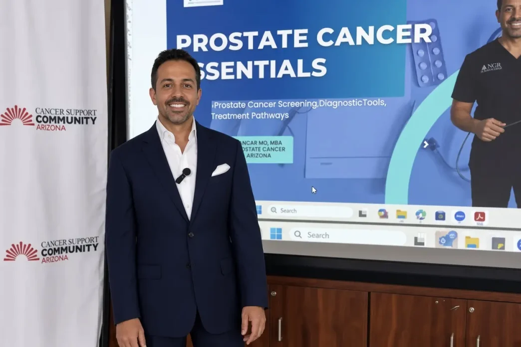 El médico oncólogo británico Ajay Bhatnagar posa en traje frente a una pantalla sobre cáncer de próstata.