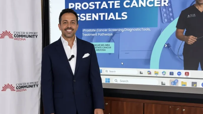 El médico oncólogo británico Ajay Bhatnagar posa en traje frente a una pantalla sobre cáncer de próstata.