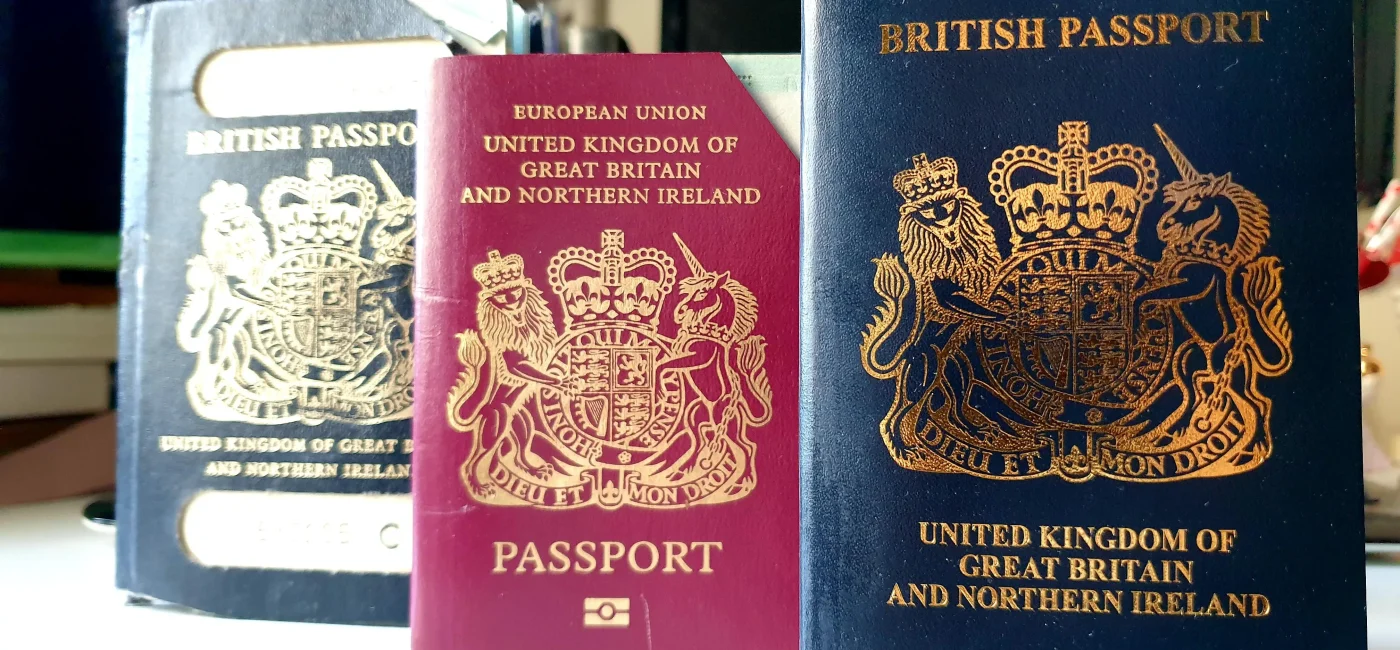 Tres pasaportes británicos de colores azul y burdeos apoyados sobre una superficie blanca.