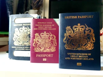 Tres pasaportes británicos de colores azul y burdeos apoyados sobre una superficie blanca.